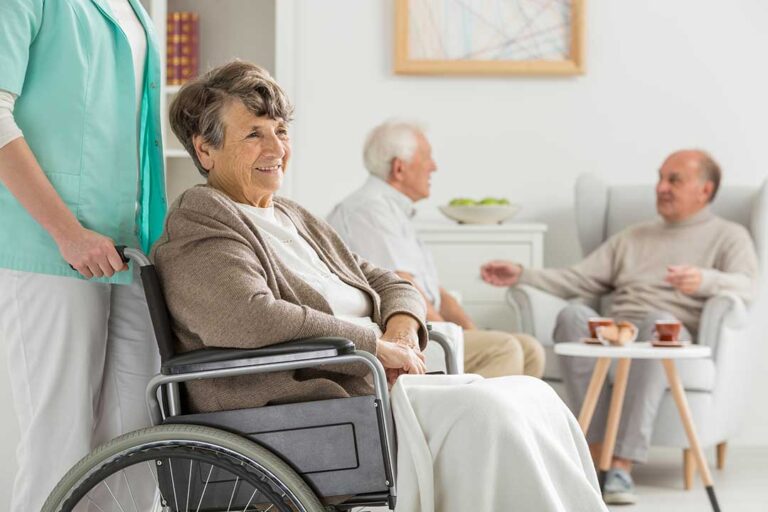 A caregiver assisting an older adult with a walker through a well-lit, furnished living room.