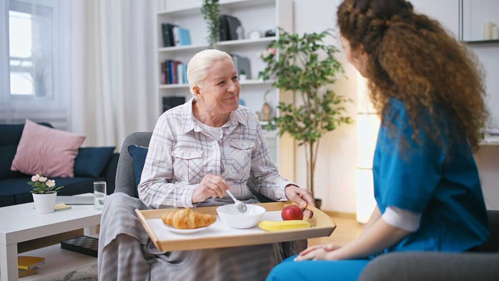 Older adults perform seated stretching and light strength exercises in a bright assisted living activity room.
