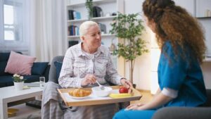 Older adults perform seated stretching and light strength exercises in a bright assisted living activity room.