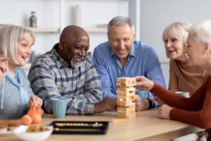 Family member sits beside an older adult during a small assisted living activity with crafts and refreshments.