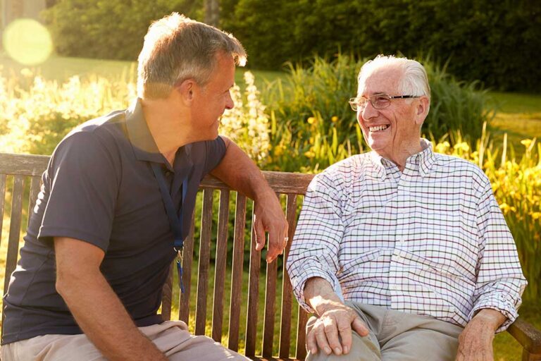Older adults participate in a gentle music and stretching activity in a bright assisted living lounge.